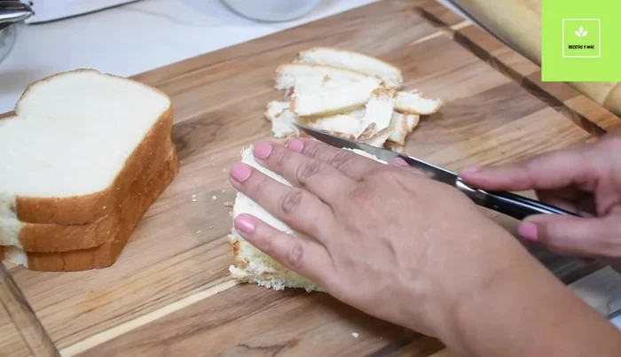 Preparación del pan relleno: Corta las orillas del pan y aplánalas. Unta cada rebanada con la pasta de mantequilla, agrega queso mozzarella, pepperoni o jamón y enrolla.