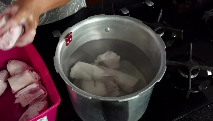 Poner a cocer las patitas de cerdo con pimienta negra, media cebolla, 3 dientes de ajo, 4 hojas de laurel y sal. Si se usa una olla de presión, cocer por 20 minutos; si es una olla normal, aproximadamente 2 horas.