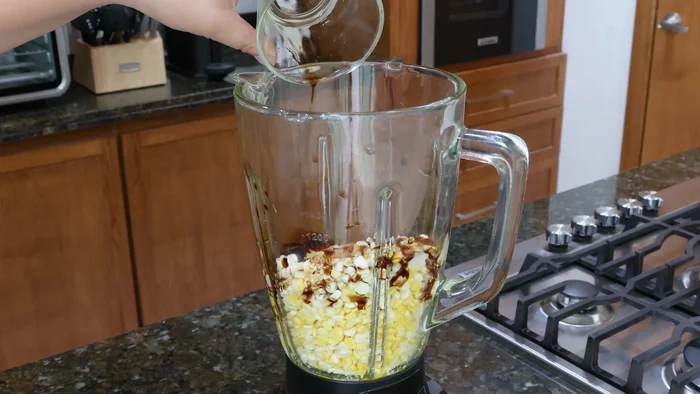 Licuar los granos de elote con leche condensada, esencia de vainilla, azúcar, jugo de naranja, huevos y polvo para hornear. Agregar una taza de leche y licuar hasta obtener una mezcla espesa.
