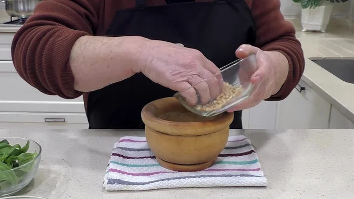Preparar el pesto: picar el ajo, añadir los piñones y la albahaca, mezclando hasta obtener una pasta. Incorporar el aceite y la mitad del queso parmesano.