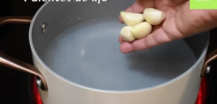 Mientras tanto, en una olla, hierve 4 tazas de agua con 4 dientes de ajo, 4 tomates, 1/2 cebolla roja, 1 cucharada de sal, 1 cucharadita de pimienta, 3 hojas de laurel, y 3 chiles guajillos tostados y sin semillas.