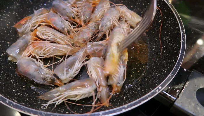Preparamos la salsa: Doramos las cabezas de langostino en una sartén, aplastándolas para extraer su jugo. Añadimos caldo de pescado y colamos.