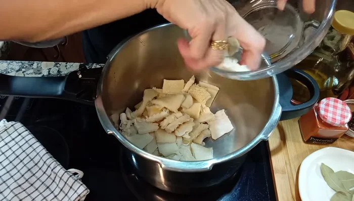 En una olla express, poner el menudo, la manita de cerdo, el chorizo, el pimiento rojo (cortado y sin semillas), la cabeza de ajo entera, las zanahorias, la patata, la cebolla, la guindilla (opcional), las hojas de laurel, la pimienta en grano, la sal, el aceite de oliva y el pimentón dulce.