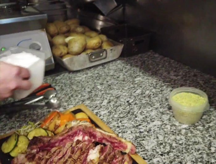 Servir el chuletón con las guarniciones, salsa de ajo con queso Manchego y praliné de pistacho (211.04).