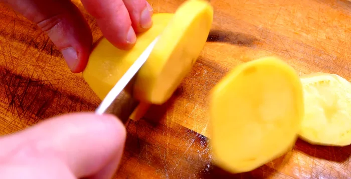 Mientras tanto, pelar y cortar las patatas en rodajas de aproximadamente 1 cm de grosor. Pelar y filetear finamente los ajos. Pelar y cortar la cebolla en juliana.