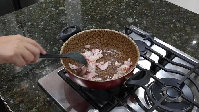 En una cacerola, freír 4 tiras de tocino en trocitos hasta que suelte su aceite. Agregar 6 cebollitas cambray y los chiles hueros.