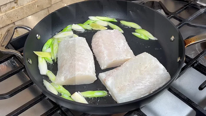 Agregar el filete de pescado a la sartén y freír durante 4 minutos por cada lado, sin moverlo. Girar la sartén ocasionalmente y revolver el jengibre y el cebollín para evitar que se quemen.