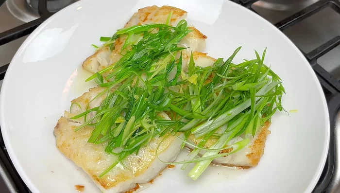 Sacar el cebollín y colocarlo sobre el pescado. Bajar el fuego, agregar salsa de soja y azúcar a la sartén. Mezclar y llevar a ebullición.
