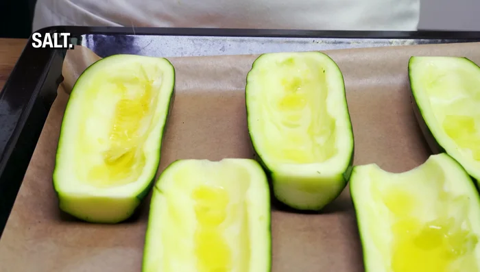 Colocar las mitades de calabacín en una bandeja para hornear con papel pergamino, rociar con aceite de oliva y espolvorear con sal, pimentón, ajo seco y eneldo seco.