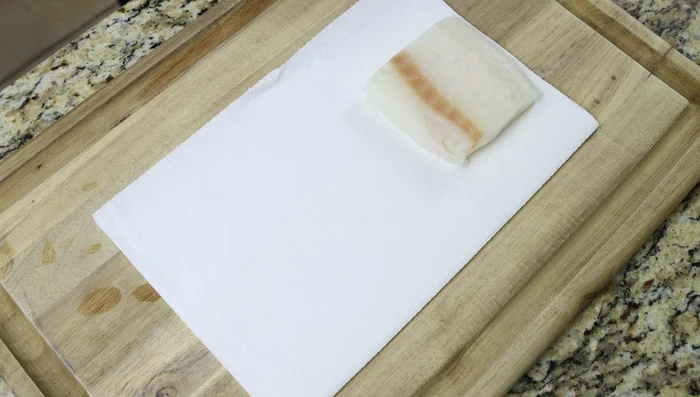 Secar los filetes de bacalao con papel absorbente, sazonar y cortar en trozos pequeños.