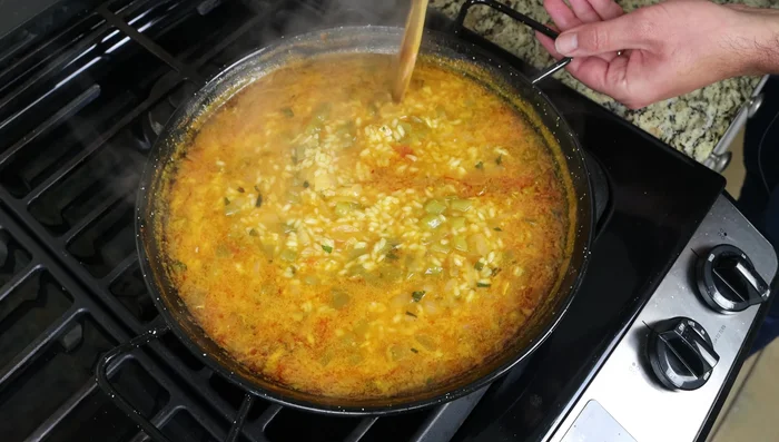 Después de 13 minutos de cocción del arroz, añadir los trozos de bacalao y los guisantes. Cocer a fuego lento durante 5 minutos más.