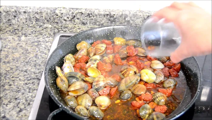 Agregar el vino blanco, sal, mezclar y dejar evaporar el alcohol hasta que las almejas se abran.