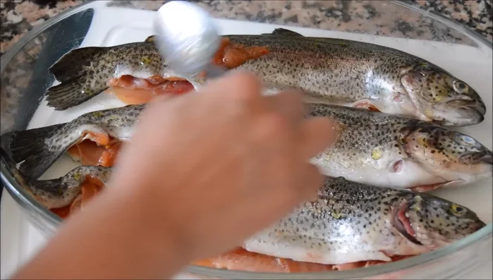 Añadir unas gotas de aceite de oliva a las truchas, extender el tomate restante por encima y colocar las láminas de ajo y los tomates cherry. (174.519)