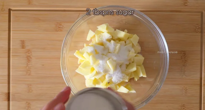 En un recipiente apto para microondas, mezclar las manzanas cortadas con 2 cucharadas de azúcar y 2 cucharadas de agua.