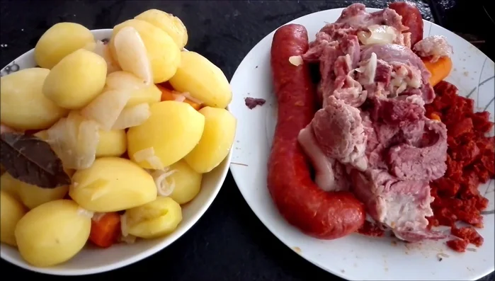 Montar el plato: colocar las patatas en rodajas como base, luego el codillo desmenuzado, el chorizo, zanahorias y pimientos.