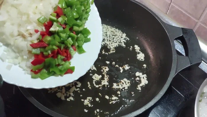 Cuando el ajo esté aromático, añadir cebolla, pimiento verde y rojo.