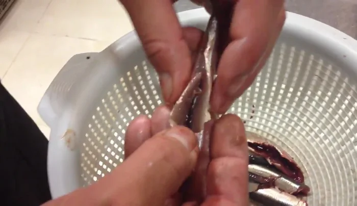 Limpiar las anchoas: sujetar con los dedos, estirar hacia abajo e introducir el dedo para sacar la tripa y la espina central con cuidado. (104.2)