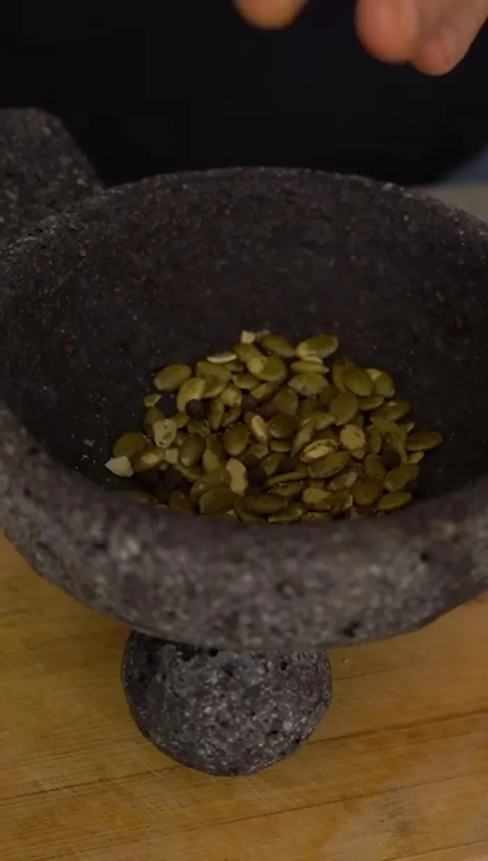 Moler en el molcajete pepitas de calabaza, pimientas enteras y sal de mar.