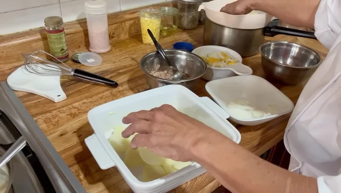 Arma el pastelón: Coloca una capa de papas en el molde. Añade capas de atún, huevo cocido y rebanado, cebolla fileteada (se puede meter al microondas 30 segundos para desflemar), y tomate. Repite las capas (312.32).