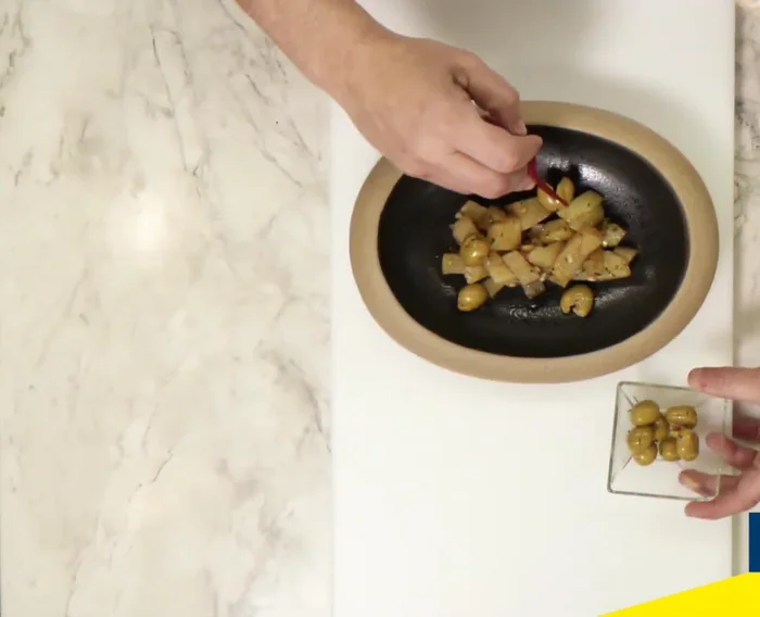 Para emplatar, hacer una base con la patata. Colocar las aceitunas aloreñas partidas, gajos de naranja pelados a vivos, lascas de bacalao, pimentón, salicornia y flores.