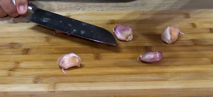 Mientras, preparar la salsa: dar golpes a los dientes de ajo, pelarlos, hacer cortes para quitar el germen y picar finamente. Reservar.