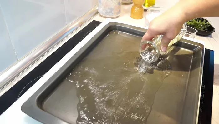 En una bandeja para horno, colocar 250 ml de vino blanco, 250 ml de agua, 1/2 cucharadita de pimienta negra en grano, 7 dientes de ajo y ramitas de romero.