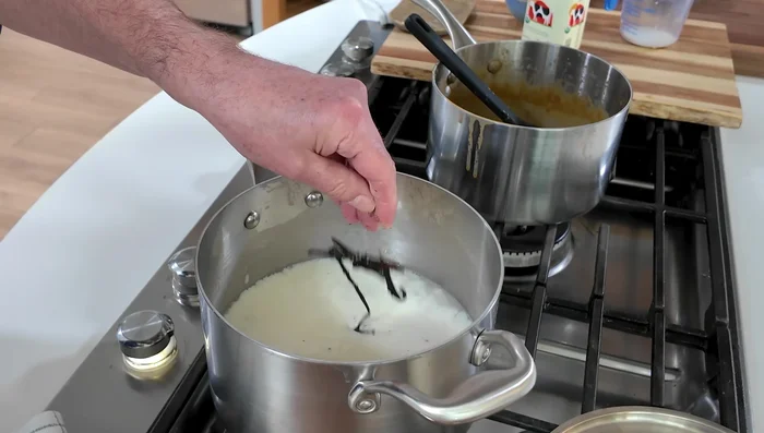 Cocinar el arroz con leche: Una vez cocido el arroz, agregar 3/4 de taza de azúcar, 2 tazas de leche con vainilla y las vainas de vainilla (141.04). Cocinar a fuego lento durante 20 minutos (149.76). Retirar las vainas y dejar enfriar (157.04).