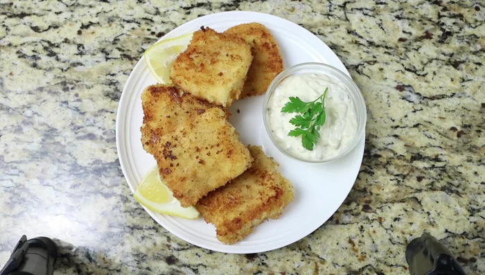Servir los filetes de pescado crujientes con la salsa tártara, rodajas de limón y perejil fresco (278.05).