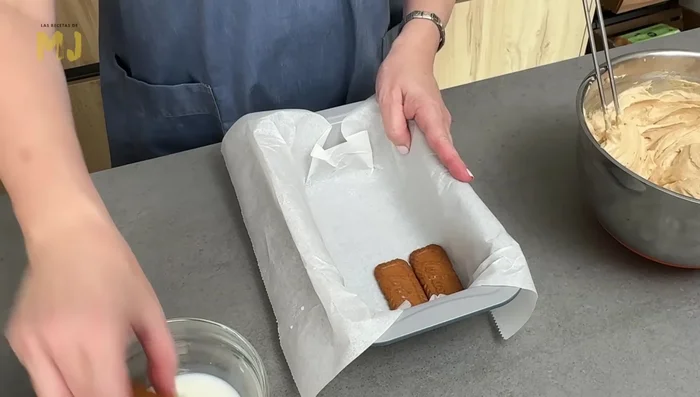 Mojar las galletas Lotus en leche y colocarlas en el molde, recortando algunas si es necesario para que encajen bien.