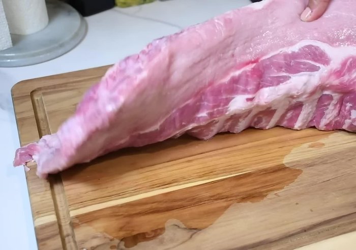 Limpiar la costilla de cerdo y quitarle la membrana de la piel. Cortarla en porciones que quepan en una bandeja.