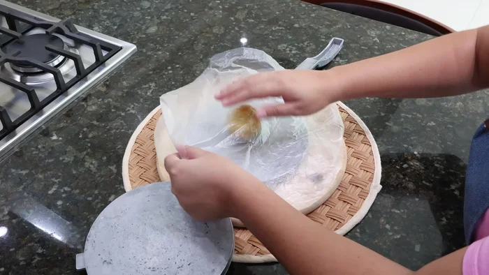 Tomar una pequeña porción de la masa y colocarla sobre una máquina para tortillas con papel plástico en ambos lados.